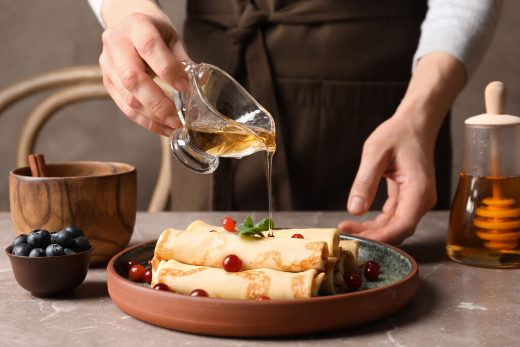 Woman,Pouring,Honey,Onto,Thin,Pancakes,With,Berries,At,Table