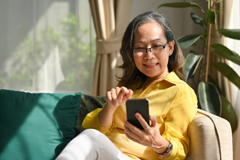 Smiling,Old,Adult,Lady,Sitting,On,Sofa,While,Enjoying,Using