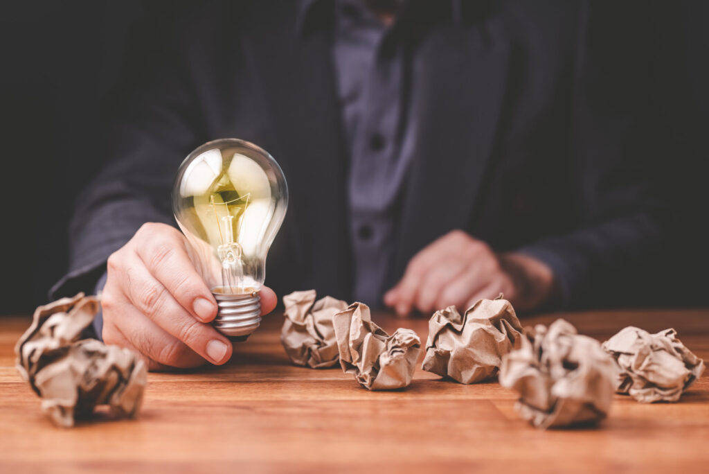 Businessman,Get,A,Glowing,Light,Bulb,Among,The,Crushed,Paper